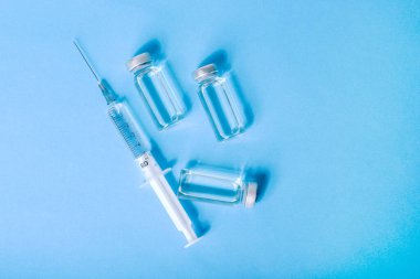 Kapsamlı aşı ve tıbbi şırınga. Mavi arka planda COVID-19 aşısı. Enfeksiyon ve hastalıkların tedavisi. Aşı klinik deneyleri