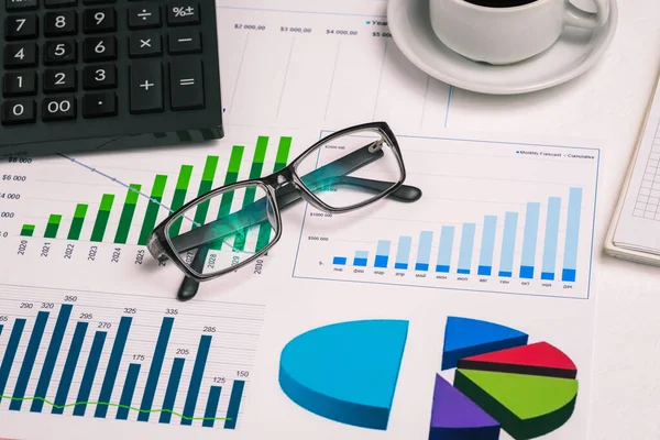 Hesap makineli, diyagramlı, bilgisayarlı, kahve fincanlı ve bardaklı bir iş yeri. Bankacılık, vergilerin hesaplanması ve şirket karları. Muhasebe ve finans.