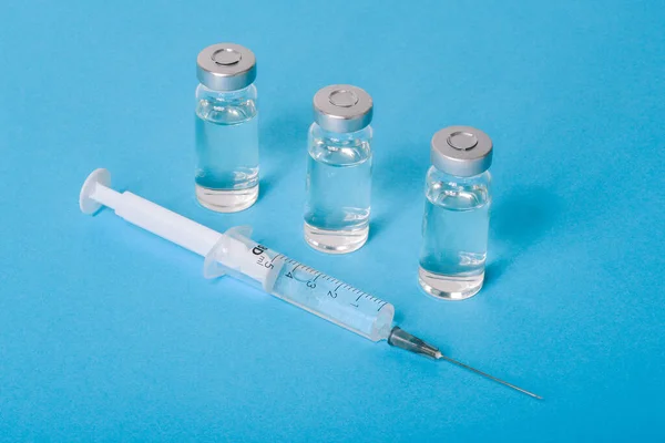 ขวดแก้วที่มีวัคซีนโควิด-19 และเข็มฉีดยาทิ้งบนพื้นหลังสีฟ้า วัคซีนป้องกันไวรัสโคโรนา การรักษาโรคและการติดเชื้อ วัคซีนของประชากร การแพทย์และการดูแลสุขภาพ รูปภาพสต็อก