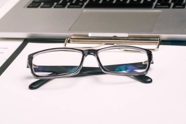 Siyah çerçeveli gözlük ve bilgisayar. Ofis çalışanı işyeri. Vergi hesaplaması, rapor ya da borsa analizi. İş konsepti