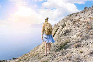 Sırt çantalı turist kız dağın tepesinde durur ve denize bakar. Gezgin ve güzel bir manzara. Gökyüzü ve dağlar. Seyahat, turizm ve aktif yaşam tarzı konsepti.