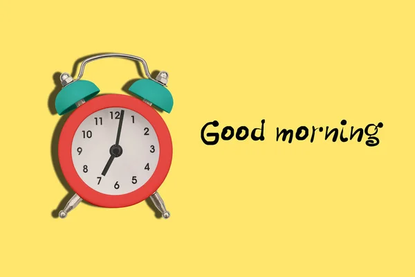 Цветной будильник на желтом фоне с тестом Доброе утро. Часы показывают семь часов утра. Пора вставать на работу. — стоковое фото