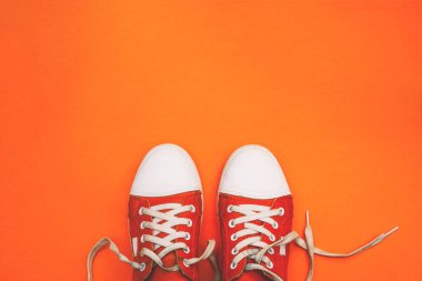 Kopya alanı olan bağcıkları çözülmüş kırmızı spor ayakkabılar. Turuncu arka planda gençlik ayakkabıları. Üst manzara, düz uzanma