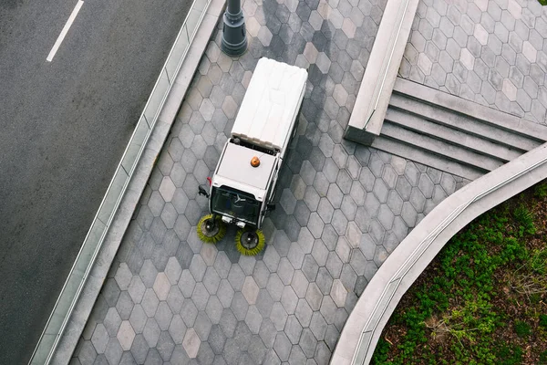 Ειδικό μηχάνημα καθαρίζει το δρόμο της πόλης από τη βρωμιά. Ένας καθαριστής με στρογγυλές βούρτσες πλένει τις πλάκες πλακόστρωσης. Η έννοια των καθαρών δρόμων από τα σκουπίδια. Άποψη από ψηλά Φωτογραφία Αρχείου