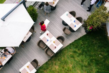 Ziyaretçilerle birlikte yazlık kafe. Yazlık verandadaki garsonun işi. Masaları ve sandalyeleri olan açık bir alan. Yukarıdan görüntüle.