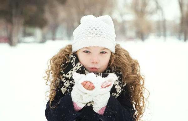 Petite fille souriant et soufflant de la neige dans un parc par temps froid — Photo