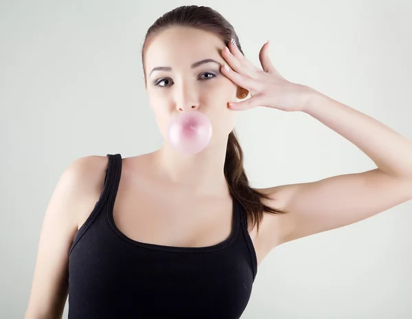 Das junge schöne Mädchen bläst eine Blase aus einem Kaugummi auf — Stockfoto