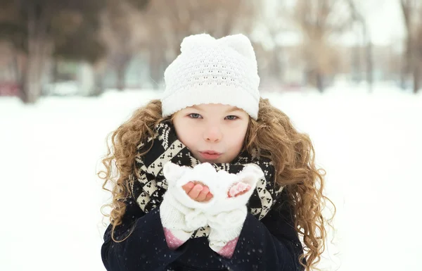 Gülümseyen ve soğuk havalarda bir parkta kar üfleme küçük kız - Stok İmaj