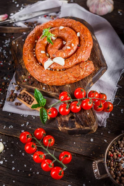 Homemade food, smoked sausage rounded with spices and cherry tomatoes, on a kitchen cutting board, dark and moody, clouseup on a black wooden isolated background, top
