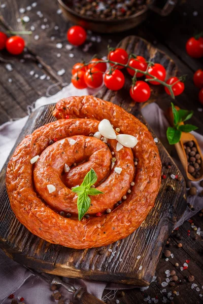 Homemade food, smoked sausage rounded with spices and cherry tomatoes, on a kitchen cutting board, dark and moody, clouseup on a black wooden isolated background, top