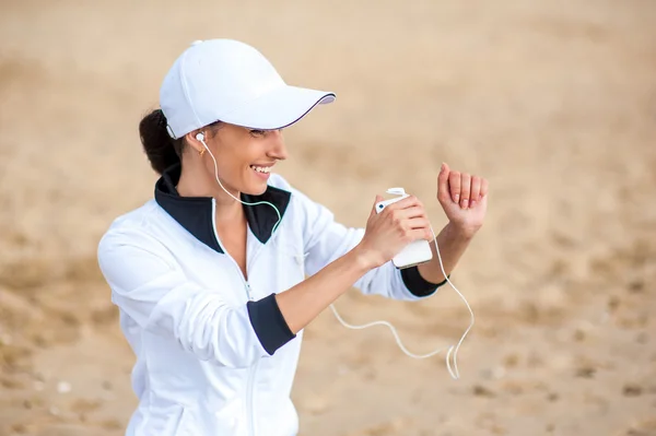 Jonge vrouw op strand luisteren naar muziek in oortelefoons van slimme telefoon mp3 speler — Stockfoto