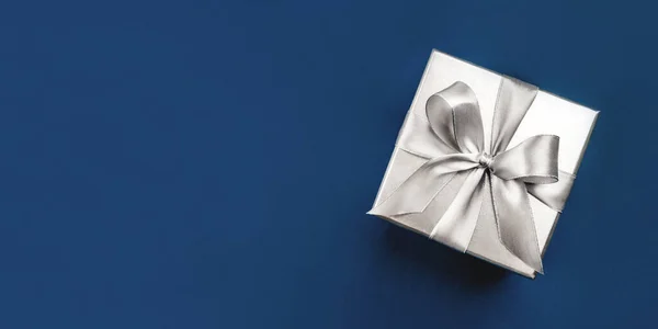 Silver gift box with bow on blue background. — Stock Photo, Image