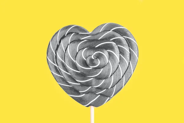 Šedé lízátko ve tvaru srdce na žlutém pozadí. — Stock fotografie