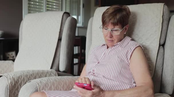 Hispânico aposentado mulher usando telefone inteligente enquanto sentado no sofá — Vídeo de Stock