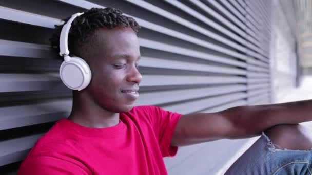 Homem africano ouvindo música de seu telefone inteligente em fones de ouvido sem fio — Vídeo de Stock