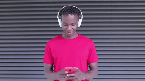 Heureux homme africain écoutant de la musique avec des écouteurs tout en utilisant un téléphone mobile — Video