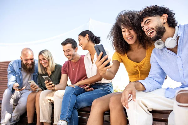 Різноманітна група щасливих друзів коледжу, використовуючи мобільний телефон, сидячи разом на відкритому повітрі - Молоді студенти дивляться обмін вмістом у соціальних мережах — стокове фото