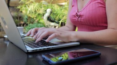 Teras restoranında otururken dizüstü bilgisayarda yazan genç bir kadının elleri.