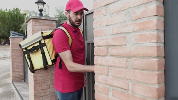 Un joven repartidor de uniforme rojo tocando el timbre para entregar un paquete — Vídeos de Stock