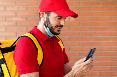 Paketleri teslim ederken cep telefonu kullanan yüz maskeli bir teslimatçı.