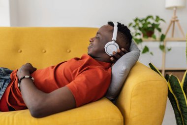 Relaxed African man lying on sofa listening to music with wireless headphones at home. listening to his favorite music and enjoying a peaceful moment at living room. Leisure concept