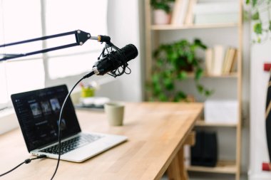 Modern podcast recording setup with microphone and laptop on desk in home studio. Creative workspace for digital media production and online broadcasting concept.