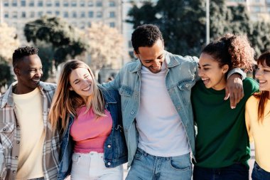 Group of millennial friends laughing while walking together at city street, enjoying time during their vacation. Friendship and youth concept