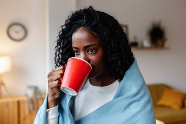 Genç yetişkin Latin Amerikalı kadın sıcak kahve fincanı tutarken evdeki pencereden dışarı bakıyor. Kış titreşimleri konsepti.