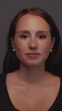 Dikey HD stüdyo fotoğrafı. Kızıl saçlı ve çilli çekici bir kadın. Kameraya ciddi ciddi bakıyor..