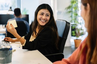 İki bayan meslektaşı, parlak, modern bir ofiste masalarında çalışırken sohbete daldılar. Üretken bir ortamda profesyoneller arasında iletişim, takım çalışması ve işbirliği.