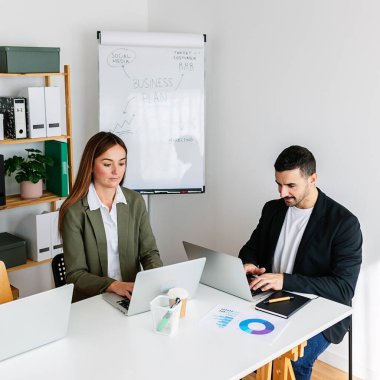 Modern bir ofiste dizüstü bilgisayarlarla iş birliği yapan iş arkadaşları, beyaz tahtada sergilenen bir iş planına odaklanıyorlar. İş konsepti