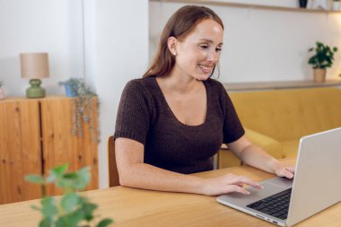 Young adult student woman using laptop computer at home. Millennial redhead female with freckles learning online. Business and education concept.