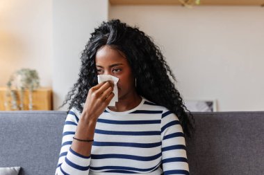 Hasta, genç, Afro-Amerikalı bir kadın, bir kanepede otururken burnunu siliyor, battaniyeyle örtülmüş, evinde kendini kötü hissediyor.