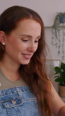 Oturma odasında bilgisayarını kullanarak internetten ders çalışan güzel bir kadının dikey HD videosu. Sahne evde uzaklık öğrenme, e-öğrenme ve öğrenci yaşam tarzını yansıtır.