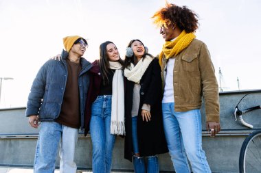 Bir grup çok ırklı arkadaş kış günü birlikte vakit geçirir, kalın kıyafetler giyer ve gülerler.