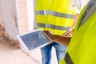 Güvenlik yelekleri mühendisleri inşaat alanındaki tabletlerin planlarını inceliyor, takım çalışması ve inşaat endüstrisinde yenilik sergiliyorlar. Mühendislik ve mimari kavramı