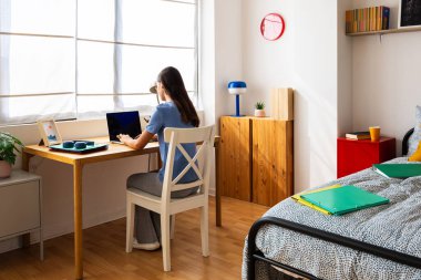 Yatak odasında dizüstü bilgisayarla çalışan genç bir kızın dikiz görüntüsü. Gençlik, eğitim ve e-öğrenme kavramı