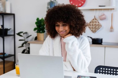 Bornozlu mutlu bir kadın sabahları evde dizüstü bilgisayarla çalışıyor.