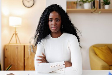 Kendinden emin Afro-Amerikan bir kadının portresi. Evdeki masada oturan kameraya bakıyor..