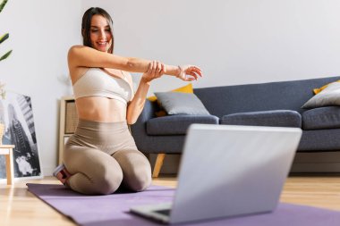 Genç ve güzel bir kadın dizüstü bilgisayarda spor yapıyor ve video dersleri izliyor. Sağlıklı yaşam tarzı ve çevrimiçi eğitim kavramı