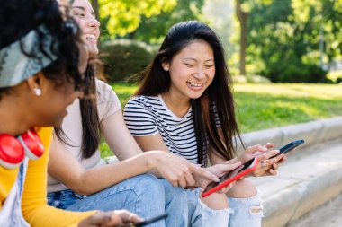 Şehir caddesinde cep telefonu kullanan üç mutlu kadın, cep telefonu uygulamasından sosyal medya içeriğini izlerken gülüyorlar.