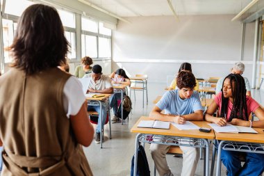 Lise öğrencileri sınav sırasında öğretmen danışmanıyla yazışıyorlar. Sınıfta sınava giren bir grup genç öğrenci. Eğitim ve öğrenim kavramı.