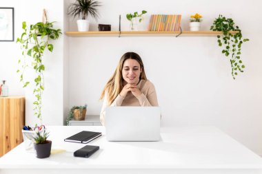 Dizüstü bilgisayardan uzak bir proje üzerinde çalışan genç bir kadın. Evde bir online toplantıya katılan odaklanmış profesyonel bir kadın. Serbest kariyer ve teknoloji konsepti.