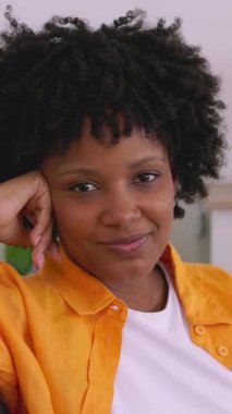 Neşeli, Afro-Amerikan bir kadının evdeki kanepede dinlenirken kameraya gülümsediği dikey HD videosu. Pozitif duygu, milenyum yaşam tarzı ve insanlar konsepti.