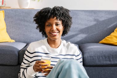 Genç Latin Amerikalı kadın kameraya gülümsüyor. Parlak bir kış gününde evde portakal suyu içiyor.