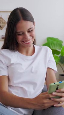 Evdeki koltukta cep telefonu kullanan mutlu genç kızın portresi. Gençlik yaşam tarzı ve sosyal medya kavramı