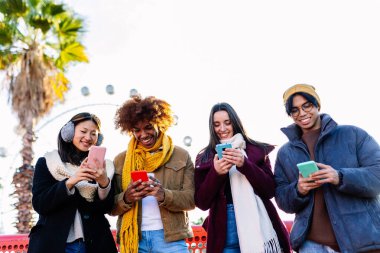 Kışın cep telefonu kullanan, kalın giysili genç bir grup insan. Sosyal medya ve teknoloji yaşam tarzı kavramı
