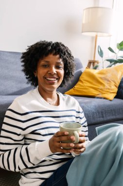 Latin Amerikalı genç bir kadının dikey portresi. Kanepede dinleniyor. Sıcak bir kış günü sıcak bir şeyler içiyor.