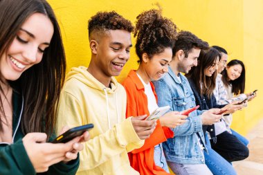 Young group of people having fun using mobile phone over yellow wall. Communication and social media concept