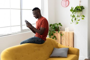 Genç mutlu Afrikalı adam evde cep telefonuyla sohbet ediyor. Sosyal medya ve iletişim yaşam tarzı kavramı